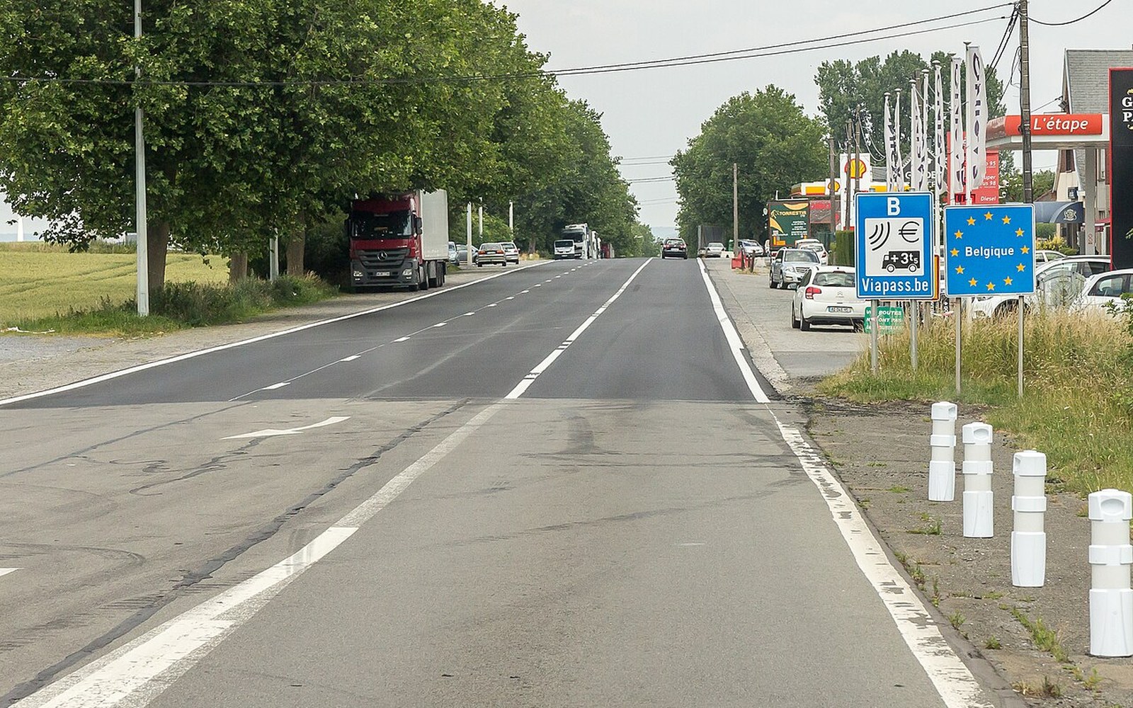 A bilingual road sign at a rural junction, the second language beneath the French, fields behind